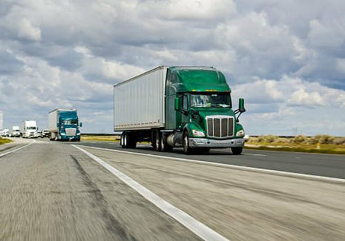 A green truck driving on Interstate 5 in California on an overcast day.